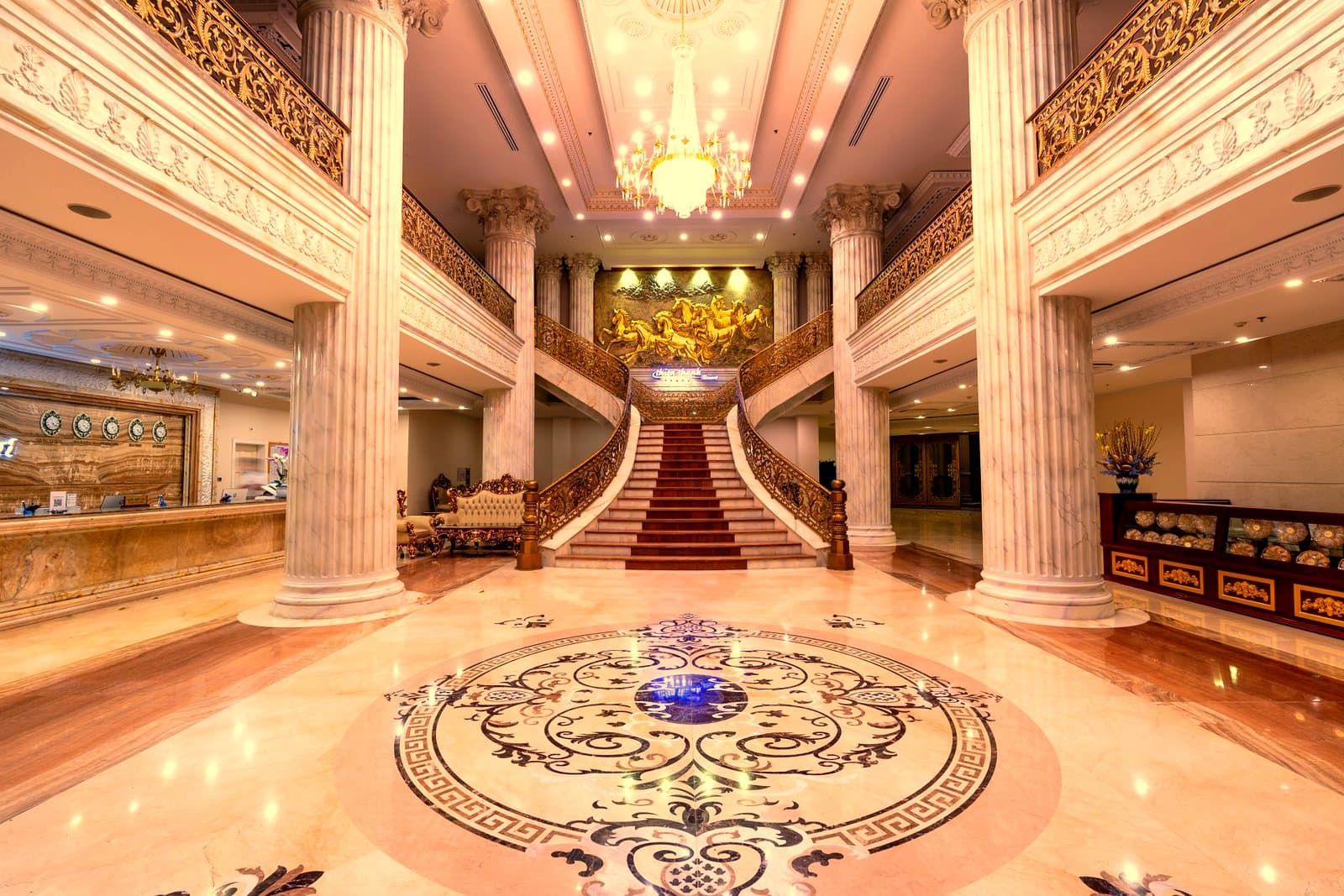 Elegant hotel foyer featuring a grand staircase, marble floors, and a dazzling chandelier.