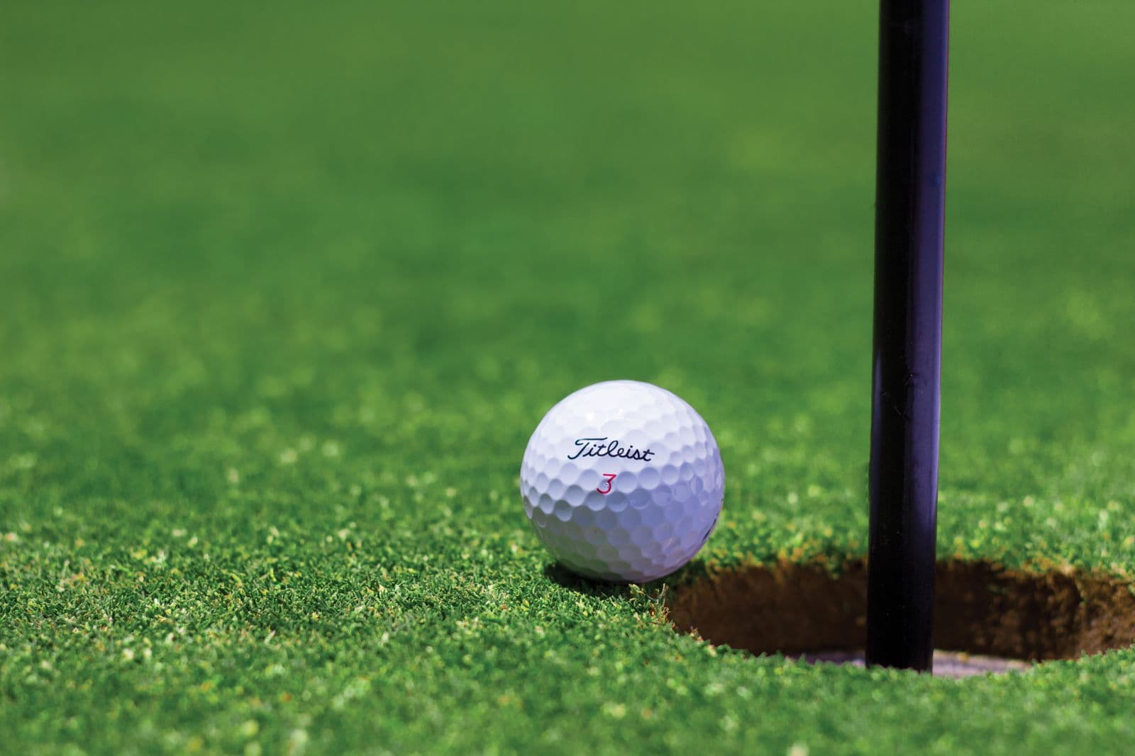 White golf ball perched at the edge of the cup on a putting green