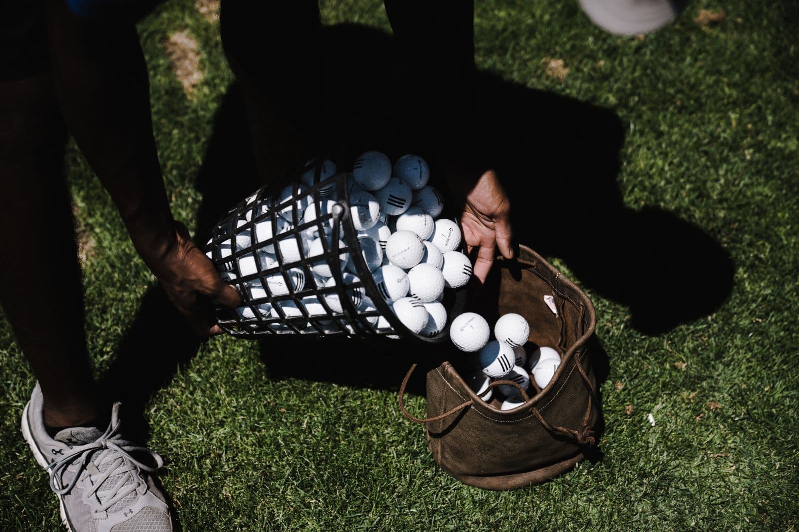 Golf balls pouring from a range basket into a canvas bag on the grass