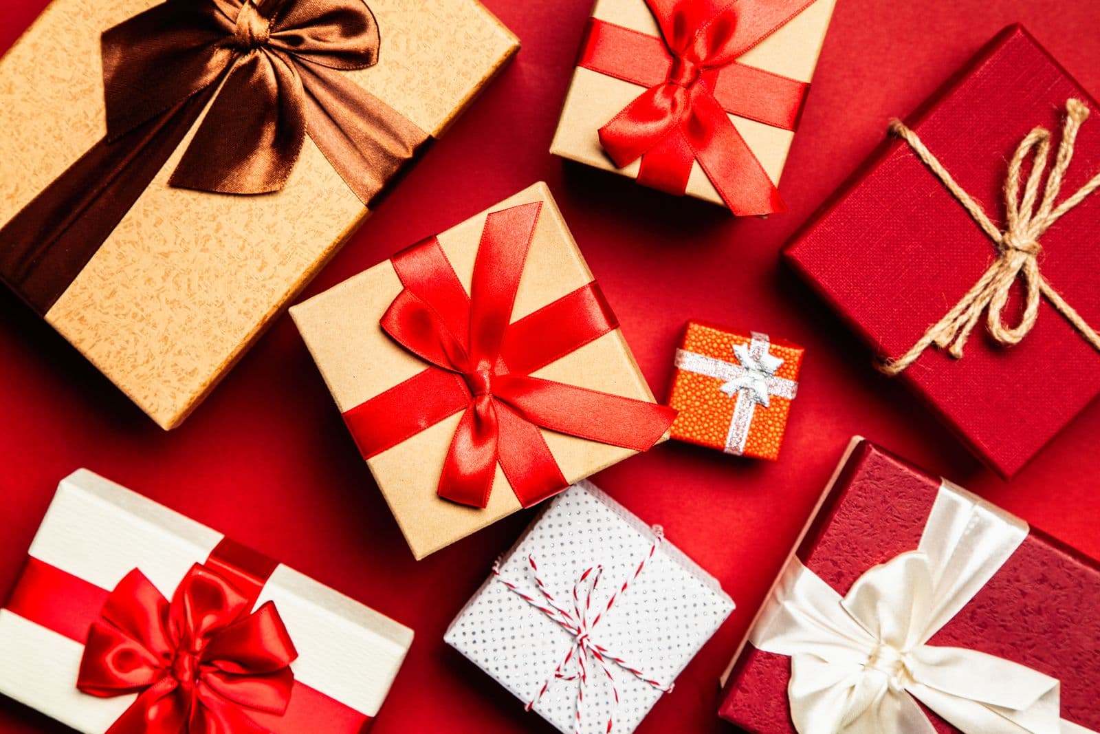 Assorted wrapped holiday gifts with satin ribbons on a festive red surface