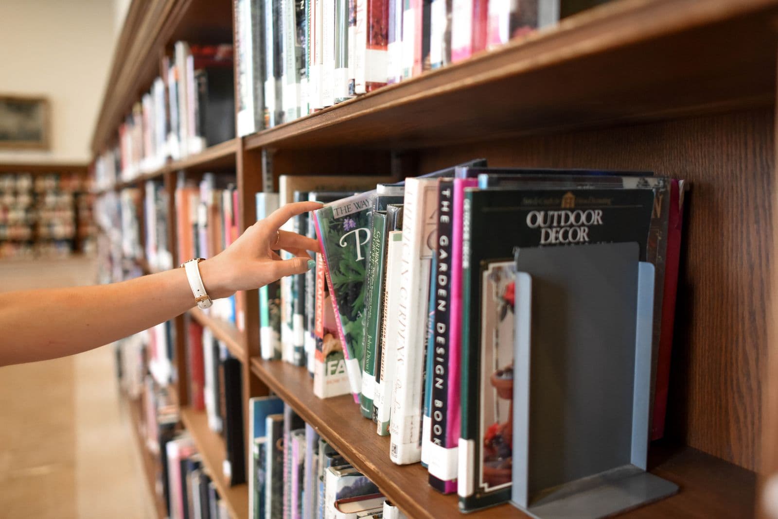 Hand selecting a design book from a polished wooden library shelf