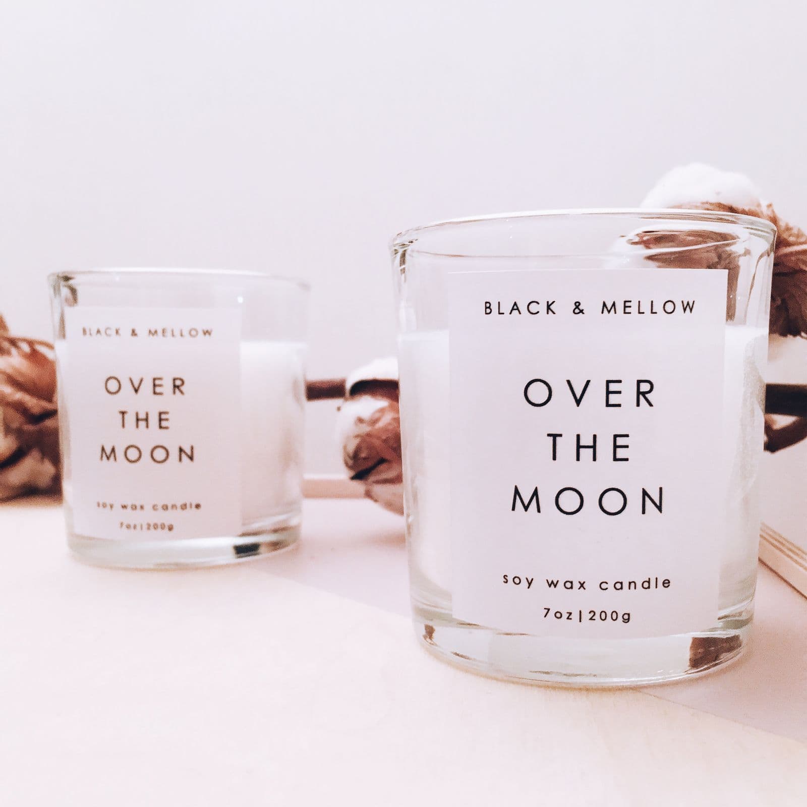 Minimal white soy candles in glass jars with dried cotton on a light surface