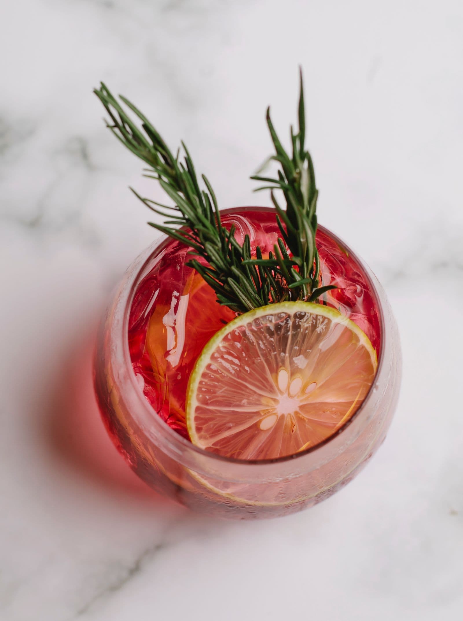 Festive red cocktail with lime and rosemary on a white marble surface