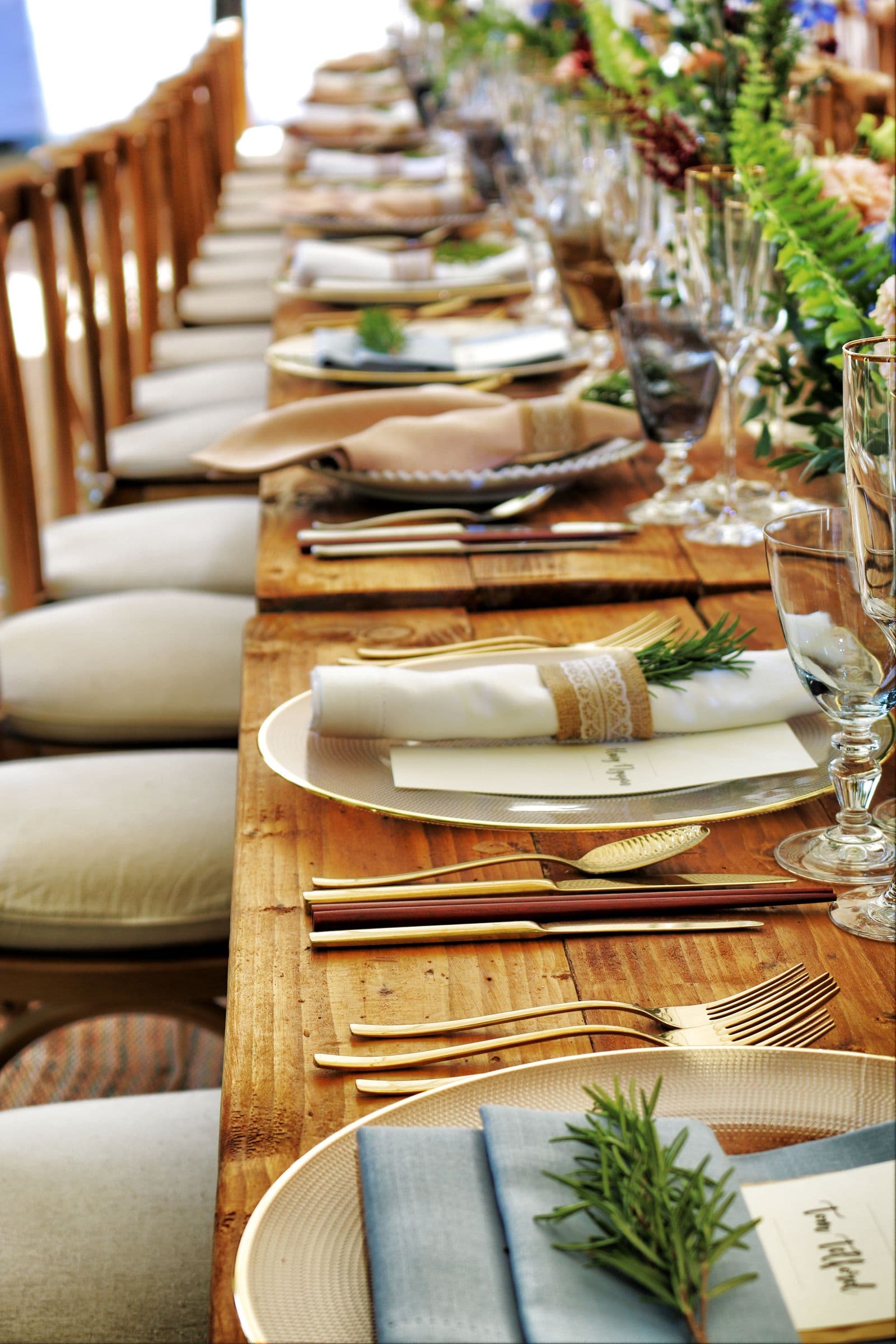 Rustic wooden dining table set with gold-rimmed plates, blue linens, and rosemary