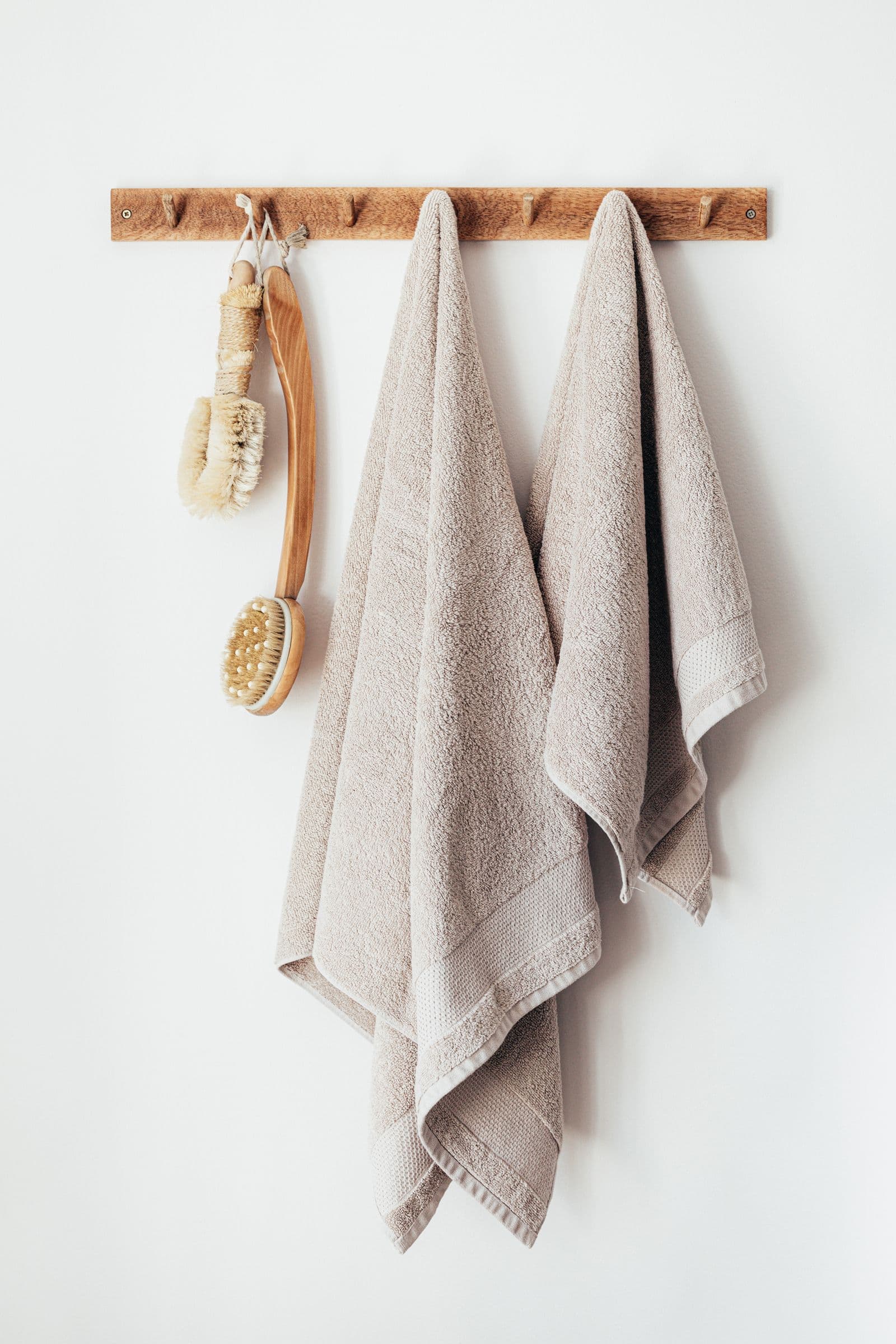 Beige spa towels and wooden bath brushes hanging on a minimalist peg rack