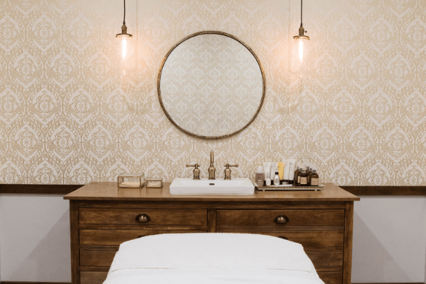 wooden vanity with round mirror and pink wallpaper